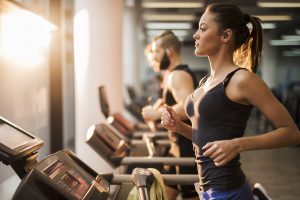 Young people exercising in a gym on treadmill. Focus is on foreground.
